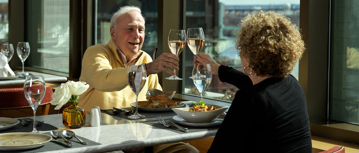 Older adult couple cheers their glasses As they enjoy a meal at their senior living community 